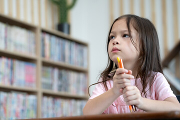 Adorable little girl back to school looking straight and holding pencil, portrait. Cute student girl child sitting at classroom desk in elementary school. Young schoolgirl education lifestyle