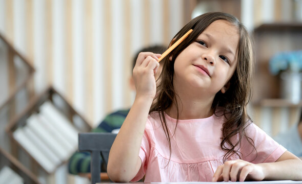 Adorable little girl happy back to school learning with paper and pencil, portrait. Cute student girl child sitting at classroom desk in elementary school smiling. Young schoolgirl education lifestyle