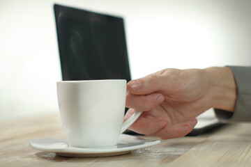 a person holding a cup with coffee on the background of a laptop
