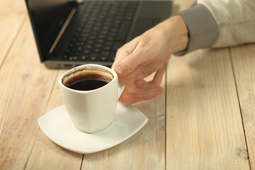 a person holding a cup with coffee on the background of a laptop 