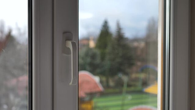 Hand of a young man closes a white plastic window at home