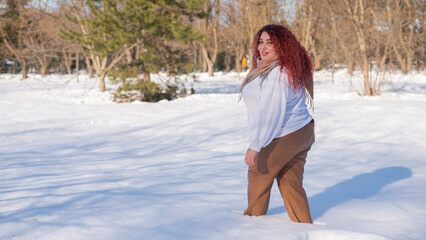 A fat red-haired woman in a white sweatshirt walks through snowdrifts. 