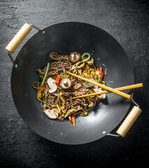 Chinese noodles wok soba in a frying pan with chopsticks.