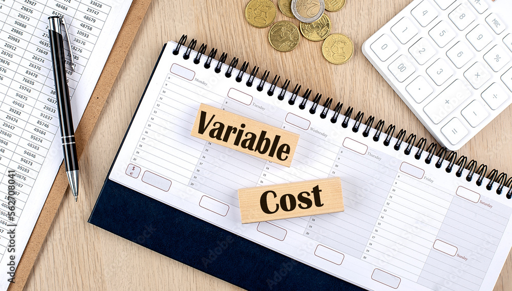 Poster variable cost word written on wooden block on planner with coins, clipboard and a calculator