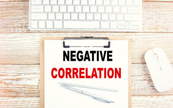 NEGATIVE CORRELATION text on a clipboard with keyboard on wooden background