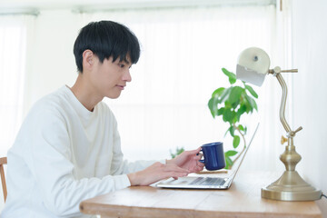 飲み物を片手にパソコンを操作する男性