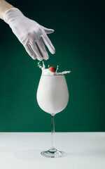 close-up of a white cocktail in a glass and a gloved woman's hand that throws a splash-creating fruit into the glass