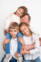 Happy loving grandfather is sitting on chair against white wall with his grandchildren on his knees