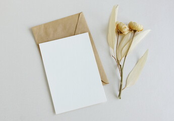 Greeting card mockup, envelope and dry eucalyptus twigs and roses on beige background top view...