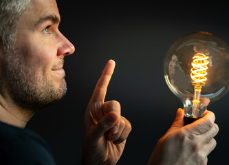 Symbol for saving energy. Man holds a filament light-bulb where the light intensity is low.