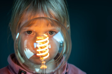 Young child looks concentrated through a filament light bulb. Symbol for a child curiously...
