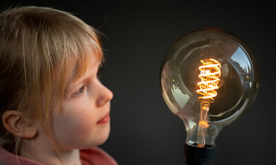 Young child looks curious to a huge filament light bulb. Symbol for a happy child discovering the...