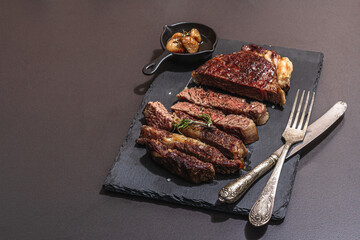 Well done roasting Ribeye steak with caramelized garlic and vintage cutlery. Hard light, dark shadow