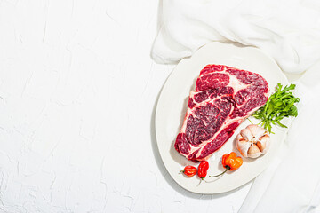 Raw Ribeye steak with spices and herbs. Dry aged meat, traditional food, hard light, dark shadow