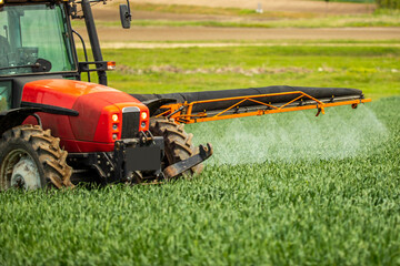 Tractor-applied herbicides, pesticides, and fungicides in wheat fields, farmer protecting crops from pests and weeds