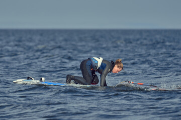 Mature woman windsurfer novice wants to raise the sail of a sailboard and continue surfing on a...