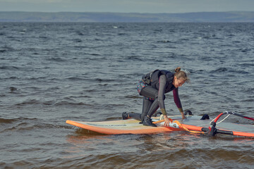 Mature woman windsurfer novice wants to raise the sail of a sailboard and continue surfing on a sunny autumn day.