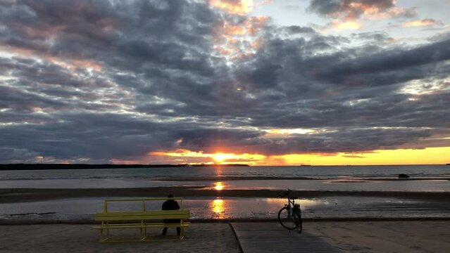 Person sitting on bench at beach ad looking to sunset. Bicycle standing beside
