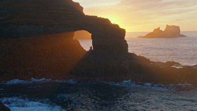 Rays of setting sun break through a hole in the rock off the coast of the Atlantic Ocean on La Palma island, Canary. Great sunset at ocean coast, aerial view. Poris de Candelaria viewpoint, La Palma