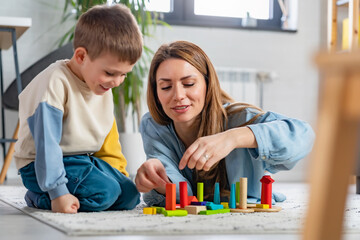 Mother and her son playing on the floor with colorful didactic toys at home. Early education and development 