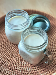 Obraz na płótnie Canvas 2 Two glasses of mason jars with natural homemade plain yoghurt, yogurt, on the handwoven rattan tray, wicker basket, high angle view. Soft theme color Korean cafe style, vertical