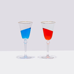 Two colorful cocktail glasses stand straight with the drink in them at an inclined angle. Surreal drinking culture, summer party or celebration composition.