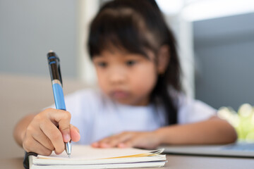 Asian girl student holding a pen for taking notes and doing homework and using the laptop for online learning class at home, Education and distance learning for children Homeschooling concept