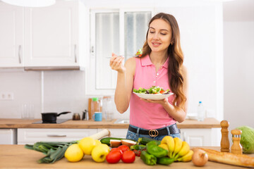 Obraz na płótnie Canvas Smiling young woman enjoying salad at home