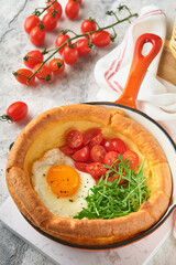 Dutch baby pancake. Fresh homemade Dutch Baby pancake with fried egg, tomato and green arugula in reed cast-iron pan on light gray concrete rustic table. Flat lay, close up.