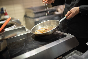 man chef cooking fried shrimp in frying pan on kitchen