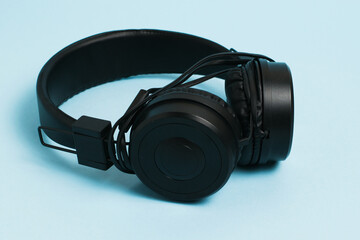 New black headphones with a wire on a light blue paper background