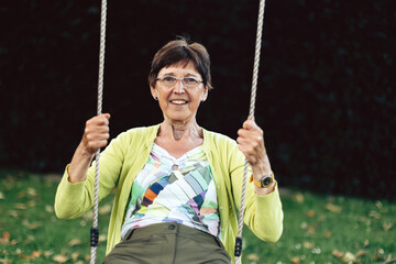 elderly woman sitting carefree on garden swing, gently rocking back and forth with a serene...