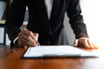 Young Asian legal advisor or lawyer reading financial details investment agreement Signing a contract for validity before the delivery of documents to help his clients succeed.