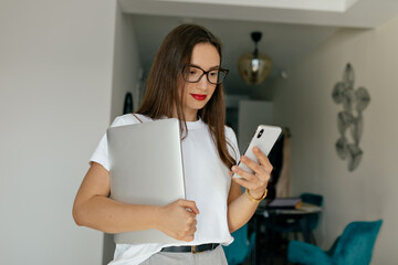 Adorable cute modern woman with dark hair and red lipstick wearing white t-shirt I using smartphone...