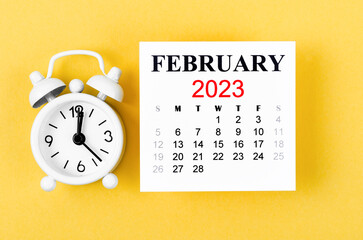 The February 2023 Monthly calendar for 2023 year with alarm clock on yellow background.