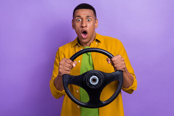 Photo of attractive young male hold steering wheel terrified frightened dressed stylish yellow look isolated on violet color background