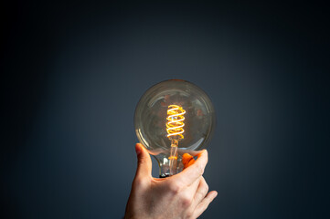 Symbol for saving energy. Hand holds a filament light-bulb where the light intensity is low.
