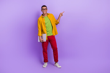 Full body portrait of cheerful handsome guy hold netbook direct finger empty space isolated on purple color background