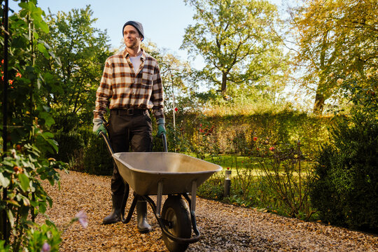 Young man walking with wheelbarrow while working in garden