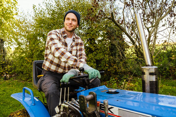 Smiling man riding lawn mower while gardening in backyard