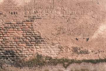 Bright brick wall with damaged brown plaster surface and moss