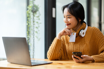 Portrait of a beautiful young businesswoman sitting at a desk holding her smartphone and credit card in data entry.