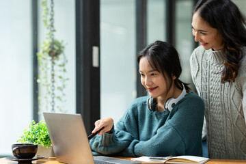 Fototapeta premium Two young Asian businesswomen discuss with smiles and joy financial management planning. New startup project ideas, and financial and statistical analysis seamlessly.