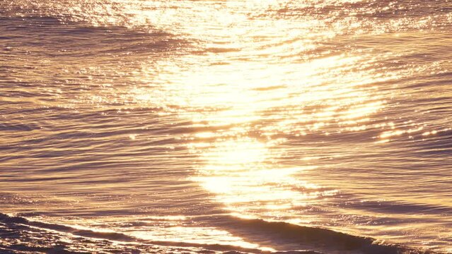 Slow motion golden ocean waves flowing with yellow sun light reflecting in a rhythmic peaceful pattern.