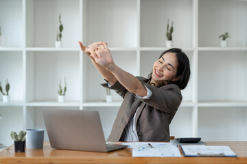A young Asian businesswoman sits in a chair relieved from fatigue as she sits in the office with a happy smile at business success.