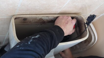 Top view of hands of plumber fitting changing toilet cistern flush siphon, handheld shot.