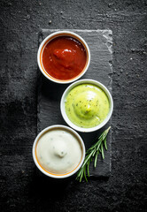 Guacomole sauce, tomato sauce and mayonnaise on a stone Board with rosemary.