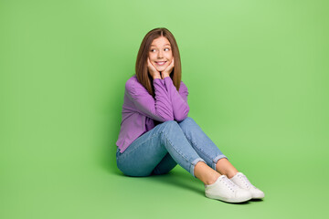 Full length photo of good mood girl with straight hairdo wear purple pullover sitting look empty space isolated on green color background