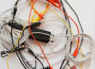 Mixed cables, node of usb cables on a white background. Yellow, orange, white and black cables from...