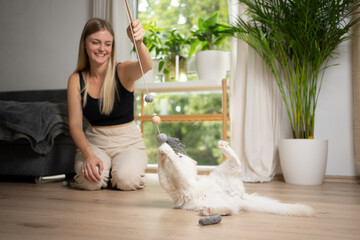 young blonde woman having fun playing with her white cat that catches a cat's toy with claws